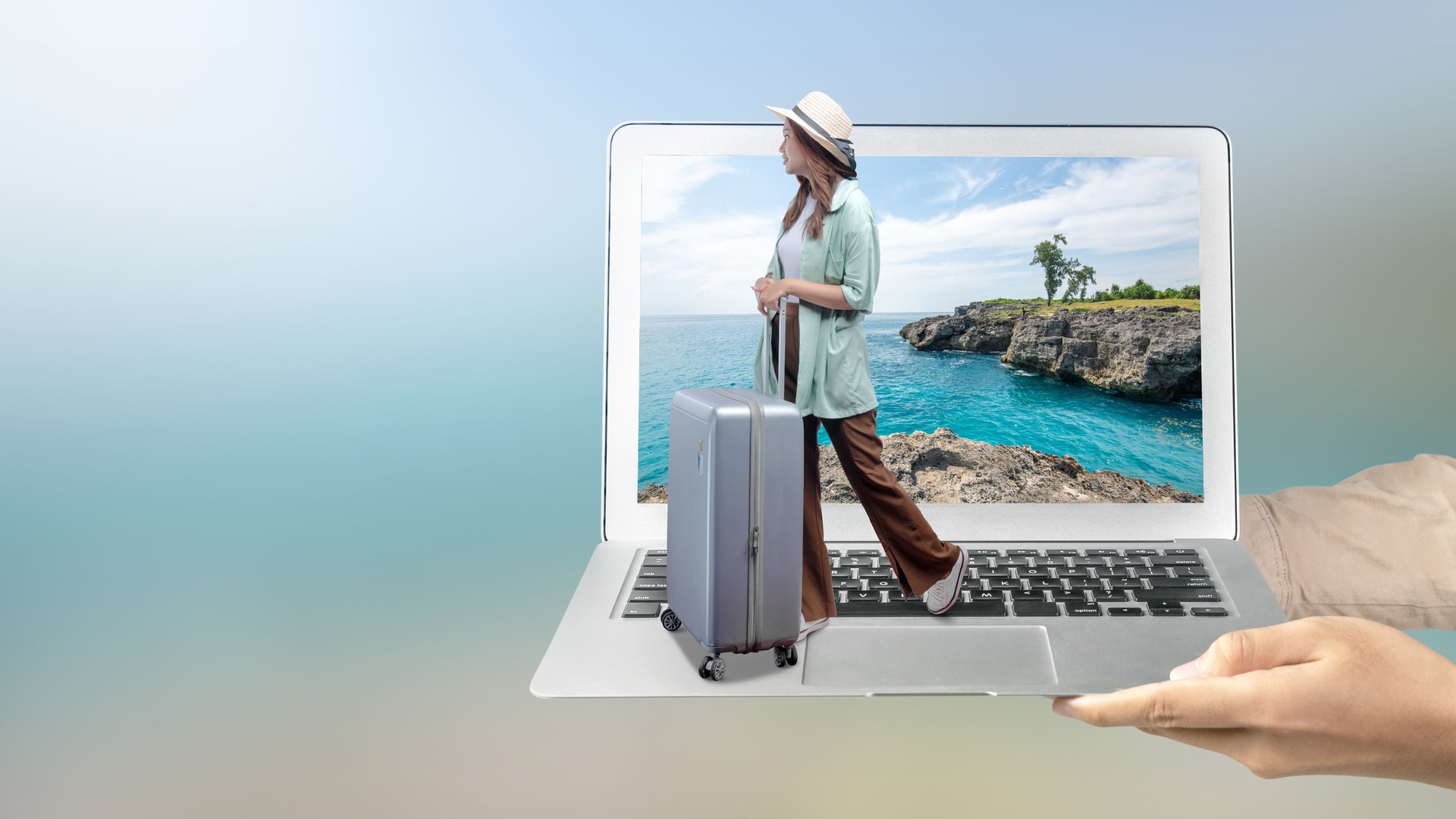 A human hand holding a laptop with an Asian girl in a hat and a suitcase with a sea cliff and an ocean view on the laptop screen